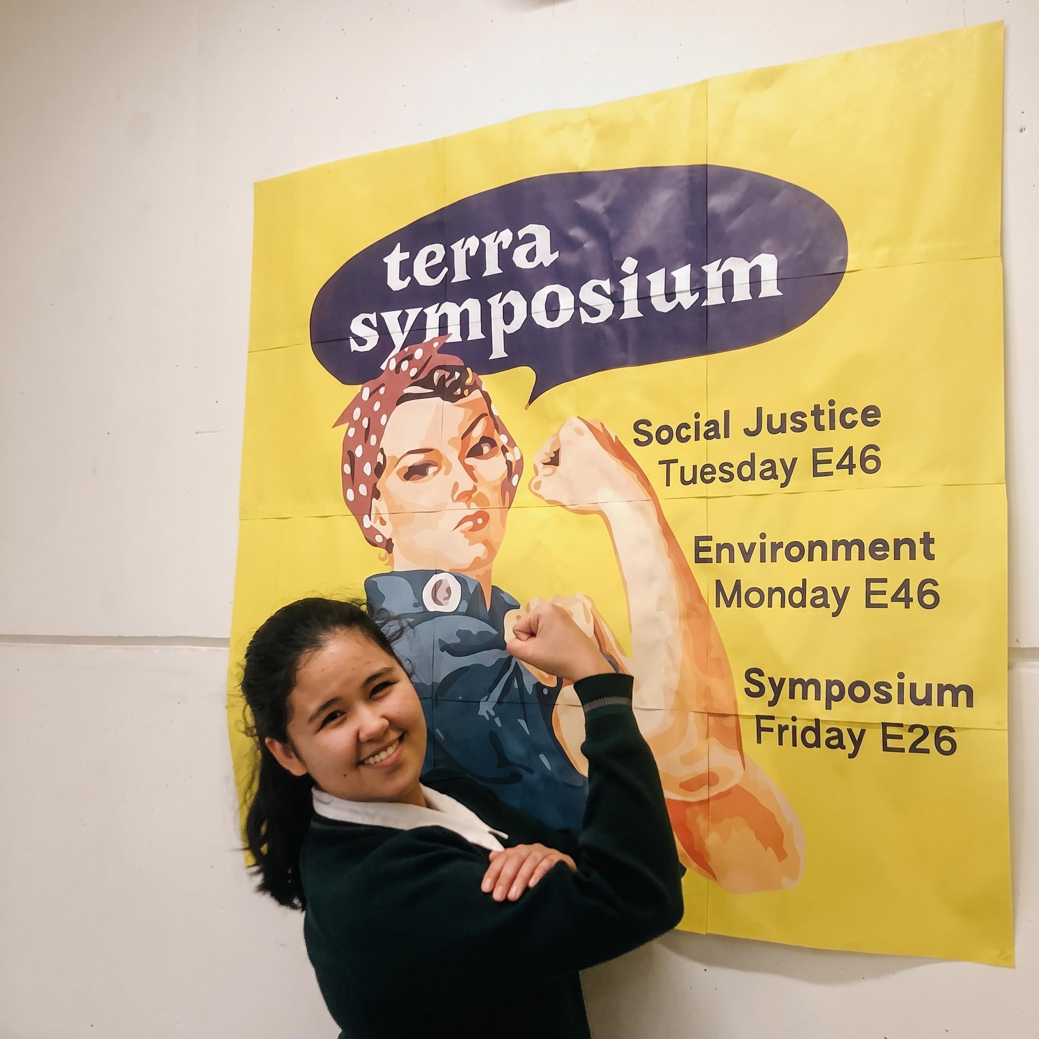 Student standing in front of a Rosie-the-Riviter Style propaganda poster, edited to advertise Terra Symposium.